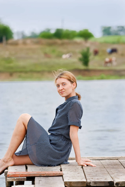 Młoda kobieta na drewnianym moście. Zielone wybrzeże z krowami na tle. - Zdjęcie, obraz