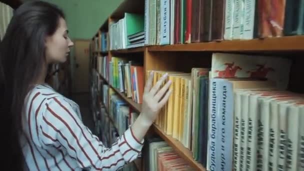 Close-up van handen slim uitziende en mooie jonge meisje in wit shirt en glazen in collage school bibliotheek selecteren boek om te lezen - Video