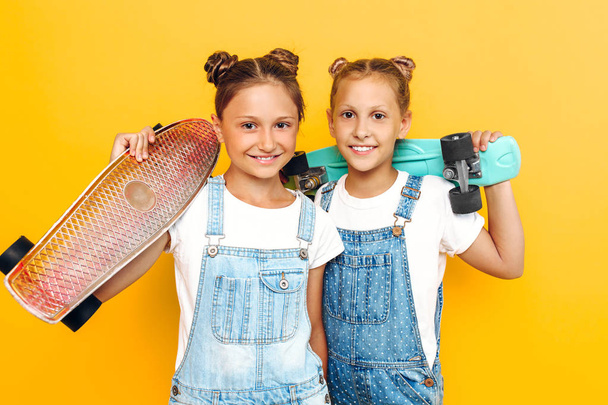 Two teenagers, stylish children posing with skateboards in their hands on a yellow background - Foto, afbeelding