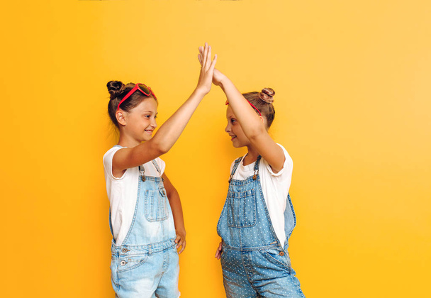 Two teenage girls, friends, greet each other on a yellow backgro - Photo, Image