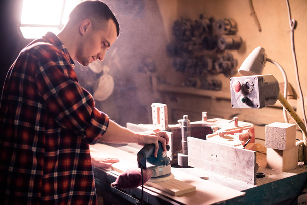 Jovem marceneiro bonito trabalhando com madeira em sua oficina de carpintaria
 - Foto, Imagem