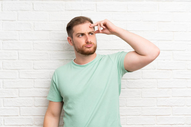 Plavovlasý muž přes cihlovou zeď s pochybnostmi a s pleznou tváří - Fotografie, Obrázek