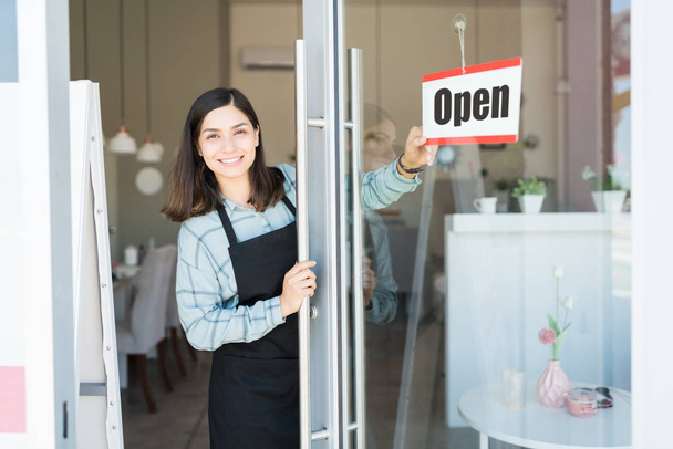 Smiling confident Latin owner turning open sign on glass door of spa - Photo, Image