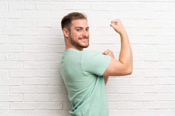Blonde man over brick wall making strong gesture - Photo, Image
