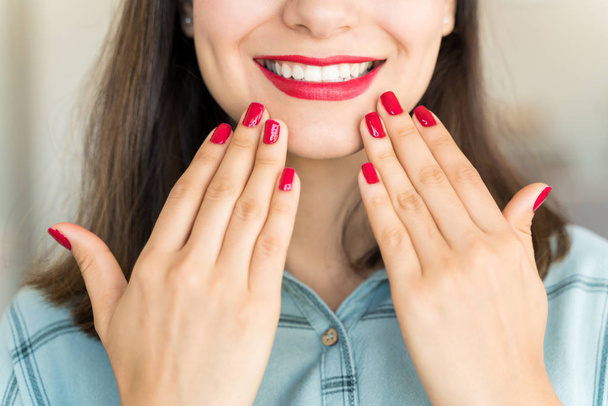 Primo piano del cliente ispanico che mostra unghie rosse e rossetto con sorriso dentato al centro benessere
 - Foto, immagini