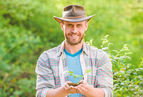 muscular ranch man in cowboy hat care plants. Eco farm worker. Earth day. happy earth day. Eco living. farming and agriculture cultivation. Gardening. successful farmer hold plant in ground in hands - Photo, image