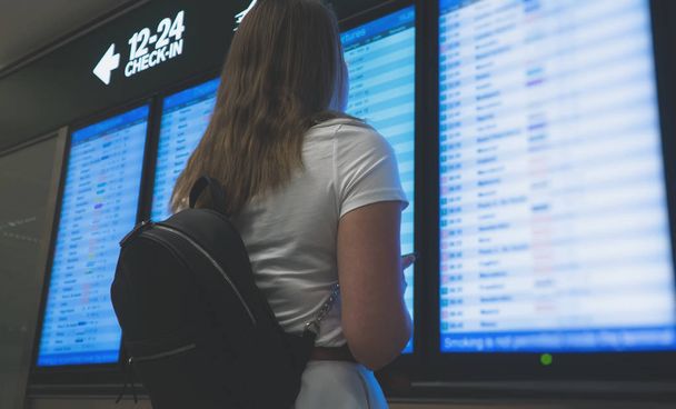 Woman in front of flight information board, checking her flight. - Photo, Image