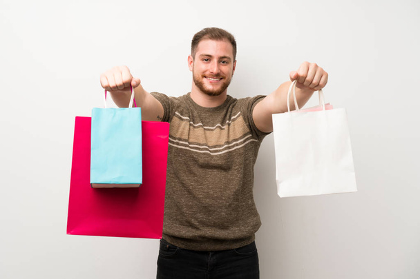 Bonito homem sobre isolado parede branca segurando um monte de sacos de compras
 - Foto, Imagem
