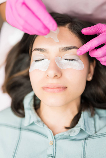 Cosmetician applying lotion over cotton pads on client's eyelids at beauty spa - Photo, Image