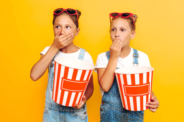 Two teenage girls, girlfriends with popcorn in their hands, watching a horror movie on a yellow background - Fotografie, Obrázek