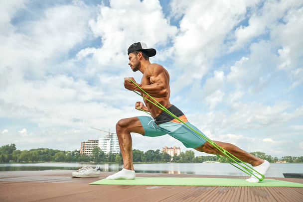 Strong man doing stretching workout in morning near lake. - Foto, Bild