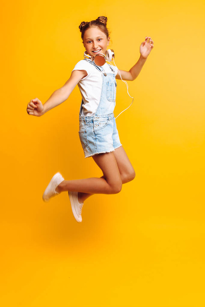 Beautiful teen girl posing with headphones over yellow background - Фото, изображение