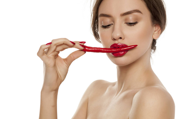 Joven mujer sexy sosteniendo un chile con sus labios sobre fondo blanco
 - Foto, Imagen