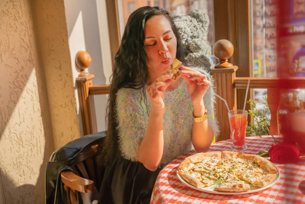 lustiges brünettes Mädchen im Pullover isst Pizza im Restaurant. - Foto, Bild