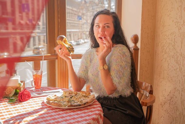 Chica morena divertida en suéter comiendo pizza en el restaurante
. - Foto, imagen