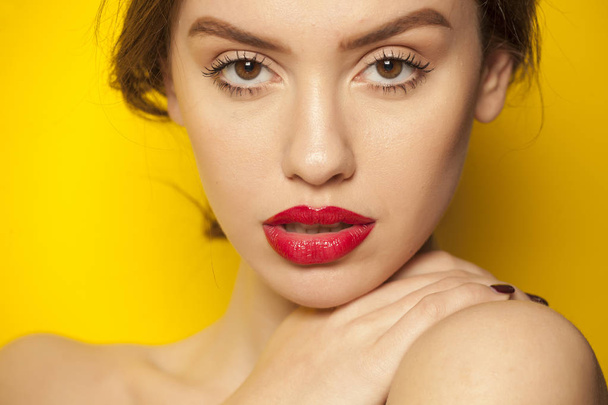 黄色の背景に、彼女の唇に赤い口紅でポーズをとる若い美しい女性 - 写真・画像