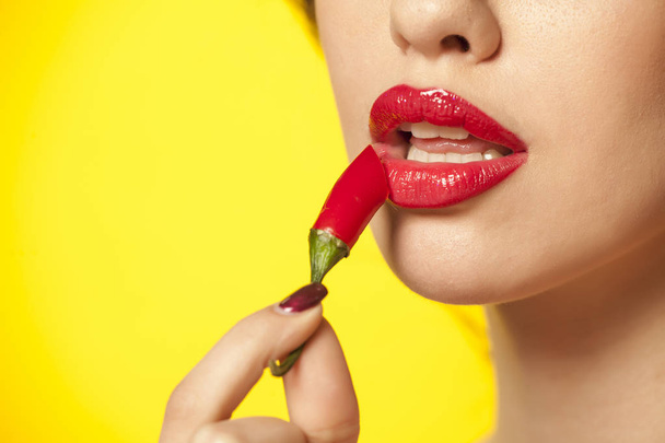 egy fiatal nő használ piros chili paprika, mint a rúzs sárga háttér - Fotó, kép