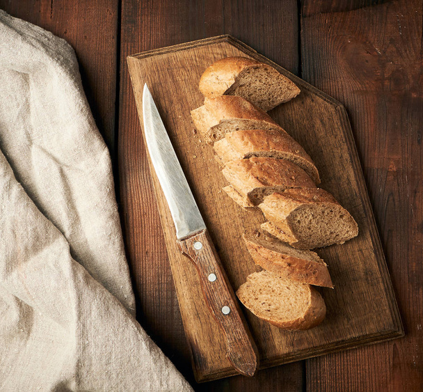 sliced rye flour baguette on a wooden cutting board - Fotó, kép