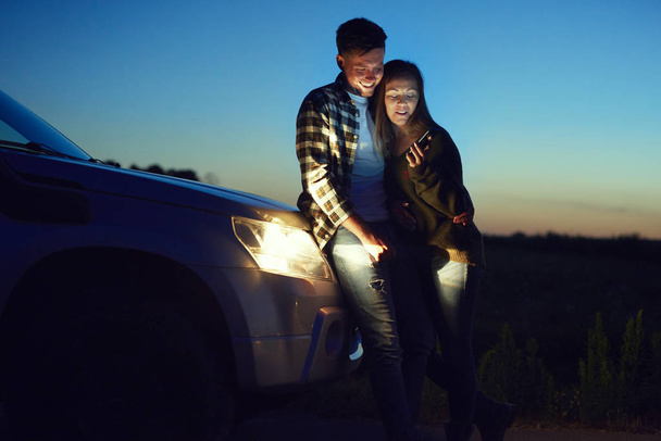 Loving couple using mobile phone during road trip at night  - Photo, Image