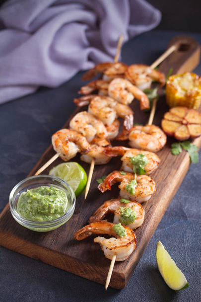 Skewered shrimps with garlic butter sauce served with cilantro and lime on serving board - Foto, Bild
