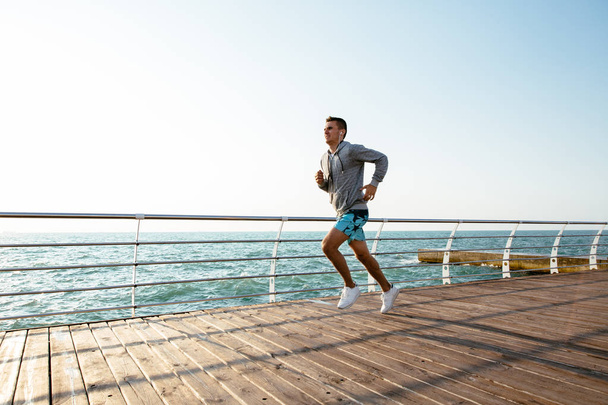 Side view of athletic guy running on quay, near the sea - Photo, Image