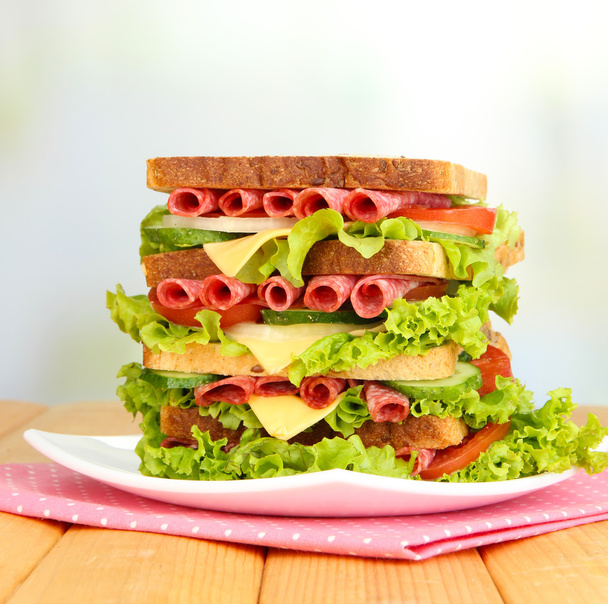 Huge sandwich on wooden table, on light background - Фото, зображення