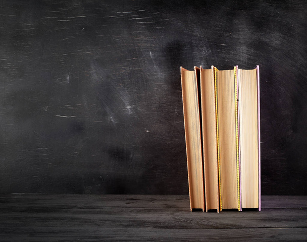 four closed books with yellow sheets on a black chalk board back - Foto, Imagem