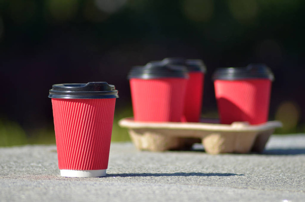 Cuatro tazas de café de papel rojo con tapas negras en un soporte sobre una superficie de hormigón sobre un fondo borroso negro
 - Foto, imagen