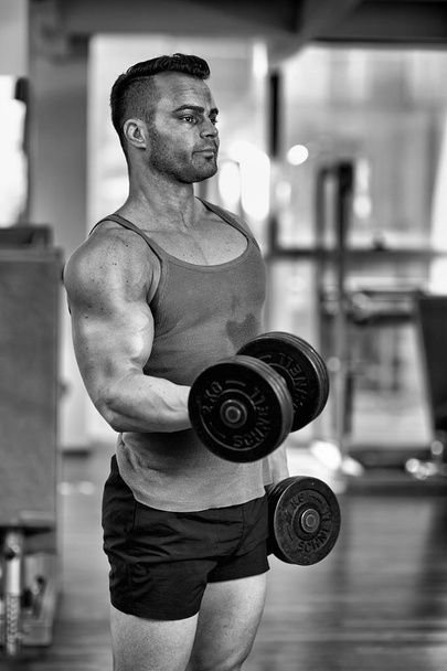 Young man doing biceps workout with dumbbells, in a modern gym - Foto, Bild