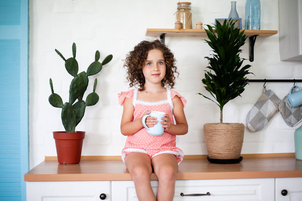 Una niña se sienta en la cocina y bebe té.
. - Foto, Imagen
