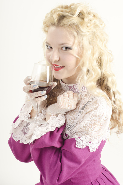 Студийный портрет красивой, привлекательной и улыбающейся девушки, одетой как старомодная леди с бокалом красного вина на белом фоне
 - Фото, изображение