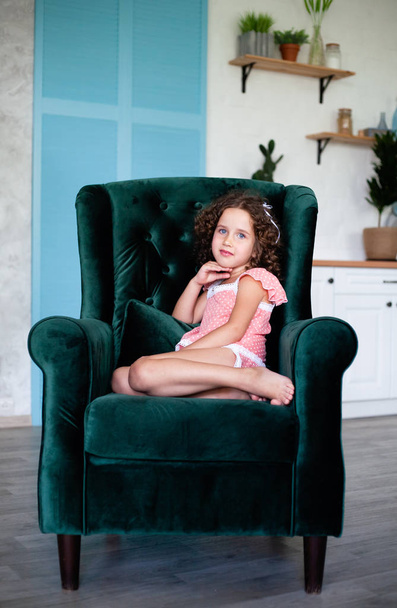 小さな女の子は大人のための大きな肘掛け椅子に座っています。ベロア, グリーン, シックなアームチェア. - 写真・画像
