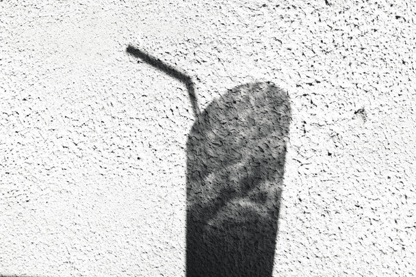 Schaduw van een glas met een drink buis op een witte muur - Foto, afbeelding
