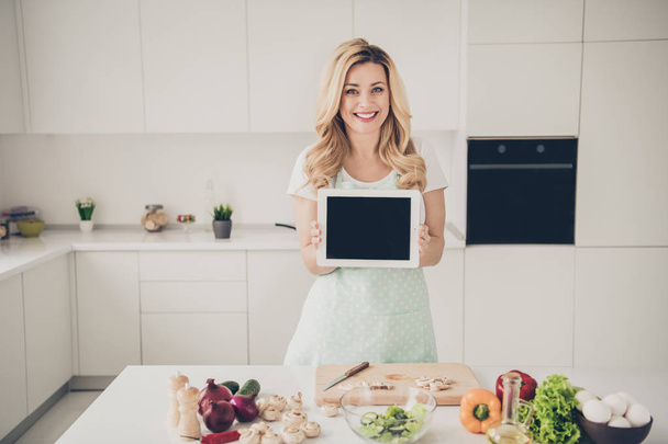 Portrait of her she nice attractive lovely experienced cheerful cheery wavy-haired lady demonstrating touch screen display making dinner in light white interior kitchen indoors - Фото, зображення