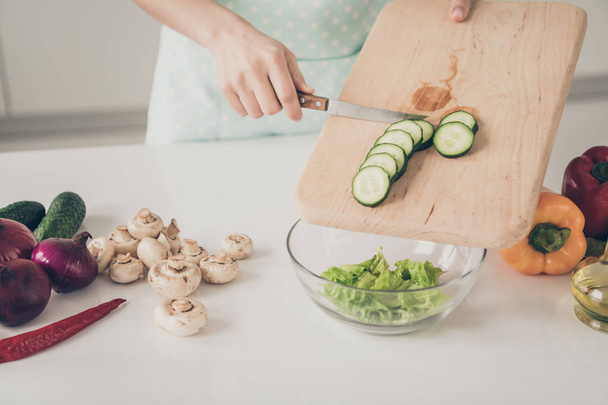 Bijgesneden foto van persoon in gestippelde schort mengen van groente putting in Bowl staande in de keuken binnenshuis - Foto, afbeelding