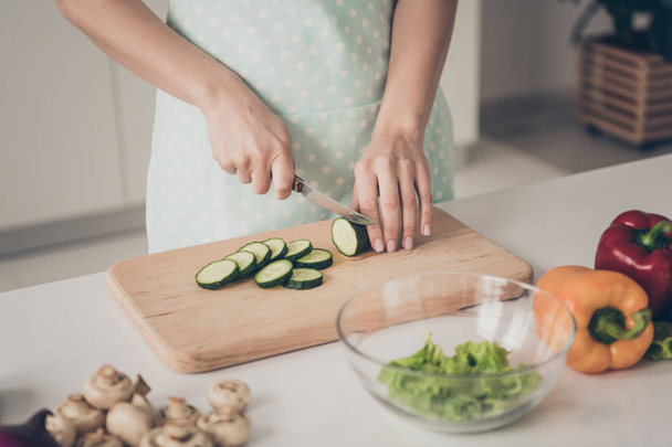 Cropped photo of person in dotted apron cutting cucumbers on desk top in kitchen - Foto, Imagem