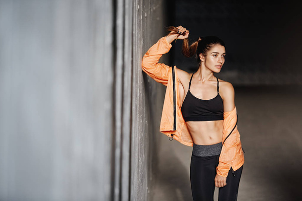 Attractive sporty girl with perfect body wear activewear leggings, lean concrete wall turn aside, smiling pleased and motivated, finish productive outdoor training session, runner prepare to marathon - Photo, image