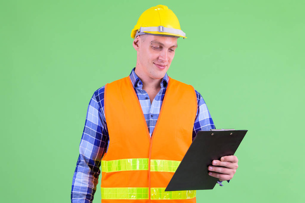 Young man construction worker reading on clipboard - Fotó, kép