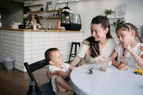 Mutter mit Kindern trinkt heiße Schokolade und Latte in einem örtlichen Café. Sie lächeln und haben Spaß. - Foto, Bild