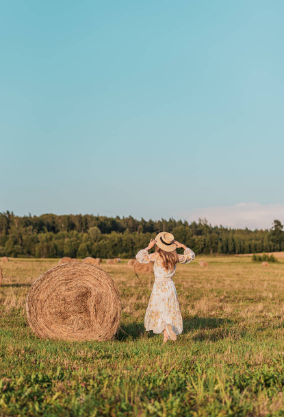 Woman walking in field with haystacks, summer time, countryside - Fotó, kép