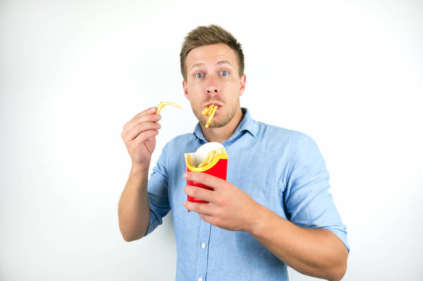 Srandovní mladý muž stojící s hranolkama v ústech na izolovaném bílém pozadí - Fotografie, Obrázek