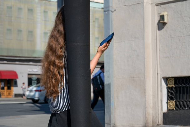 Girl with beautiful curly hair talking on a cell phone on a busy street. - 写真・画像