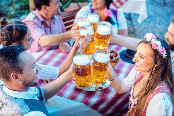 Люди, наслаждающиеся едой и напитками в баварском пивном саду
 - Фото, изображение