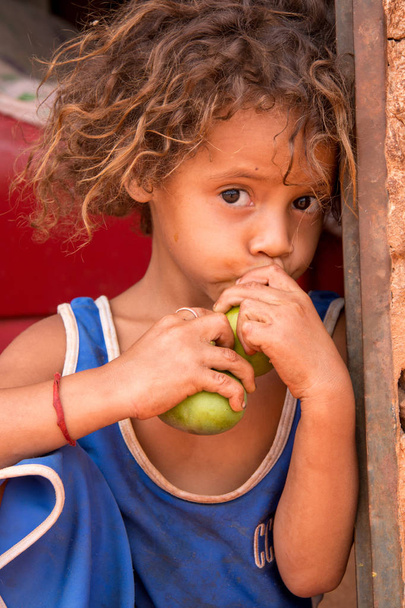 Планина, Гоа, Бразилия - 27 октября 2018 года: маленькая девочка, сидящая возле своего дома, ест манго
 - Фото, изображение
