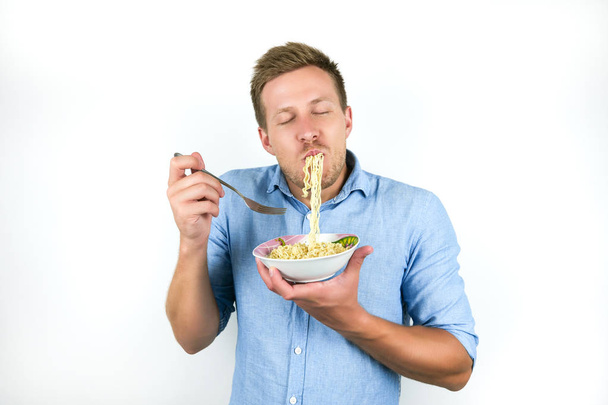 young handsome man eating noodles looks hungry on isolated white background - Zdjęcie, obraz