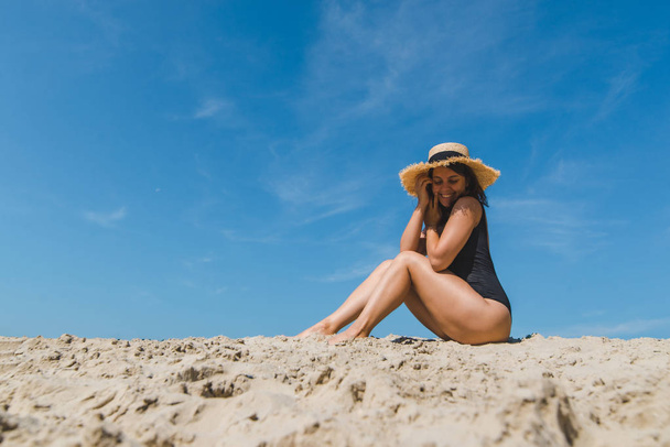 Frau am Sandstrand in schwarzem Badeanzug blauer Himmel auf Hintergrund - Foto, Bild