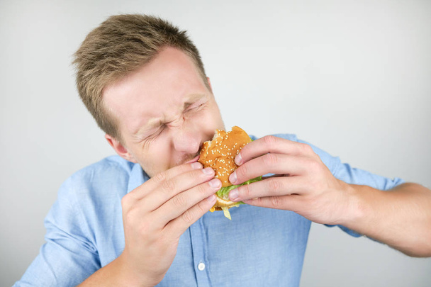 young man eats fresh tasty burger from fast food restaurant looks very hungry on isolated white background - Foto, Bild
