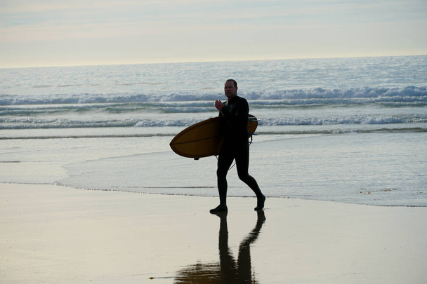 surfista de fato molhado segurando uma prancha de surf na praia durante o pôr do sol, em La Jolla Beach, San Diego, Califórnia, EUA
.  - Foto, Imagem