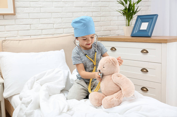 Cute child playing doctor with stuffed toy on bed in hospital ward - Φωτογραφία, εικόνα