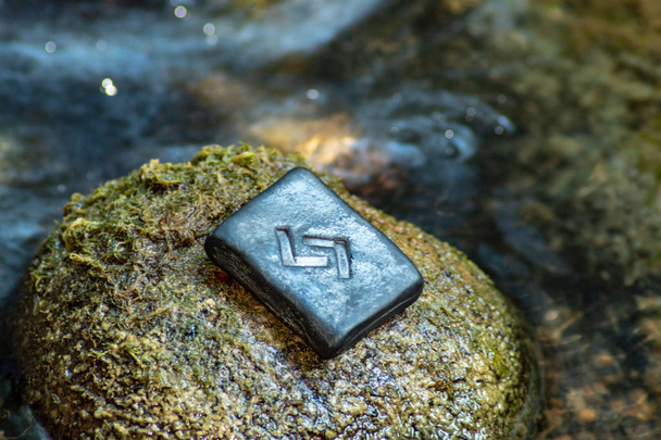 Norse rune Yera on the stone and the evening river background.  Harvest, cycle, karma. Hard work to achieve the result. - Photo, Image